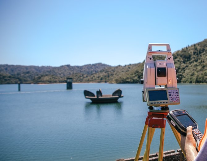 Survey equipment in foreground with dam lake in background