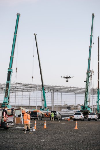 Drone in flight with large building frame and cranes in background